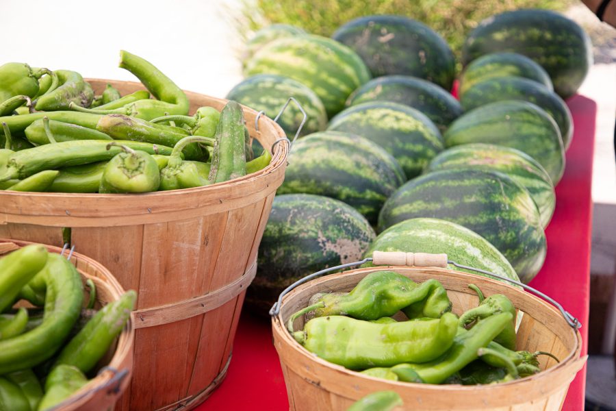 Baskets of green chile are displayed alongside watermelons at an outdoor booth.