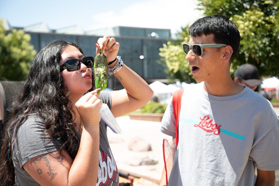 A student holds up a green chile and pretends to kiss it while another student watches in awe.