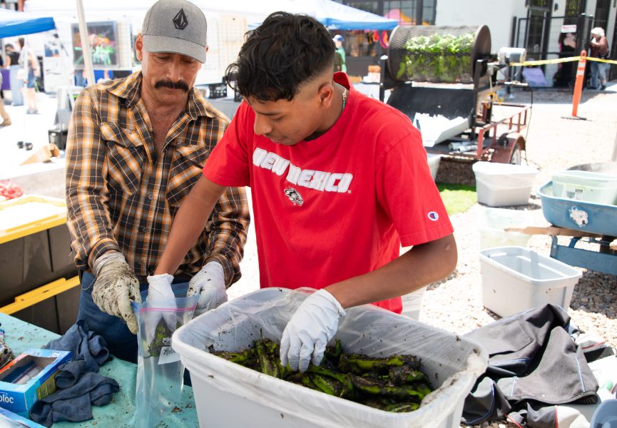 A gloved student helps a vendor to bag freshly-roasted green chile.