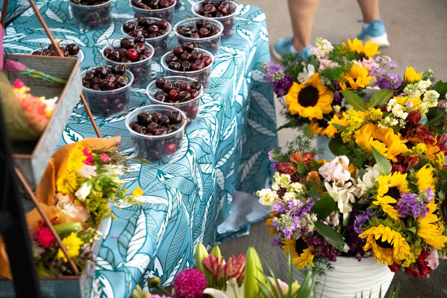 Bright floral arrangements and bowls of red cherries are presented at a booth.