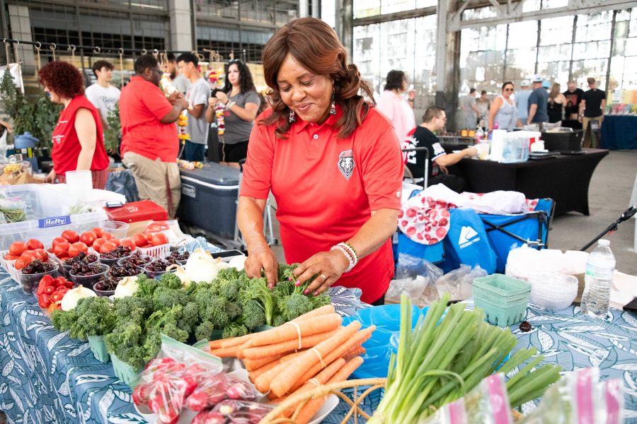 A vendor wearing UNM merchandise smiles as they tend to produce at their booth.
