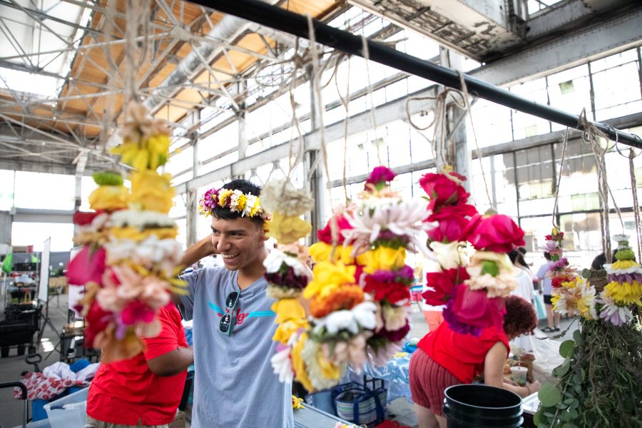 A student smiles while putting on a flower crown, framed by more florals at a Rail Yards Market booth.