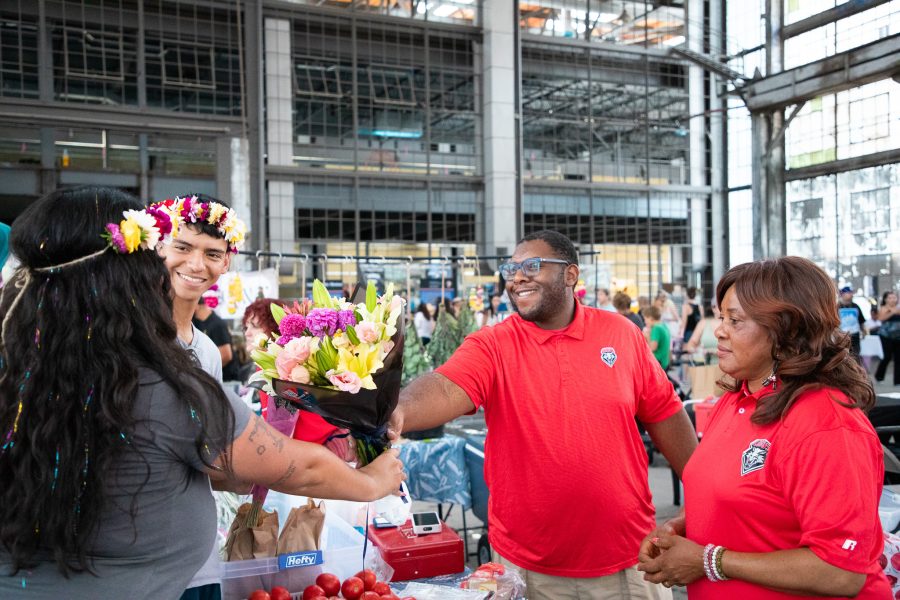 Two local business owners wearing UNM merchandise hand two students a vibrant bouquet of flowers inside the Rail Yards Market.