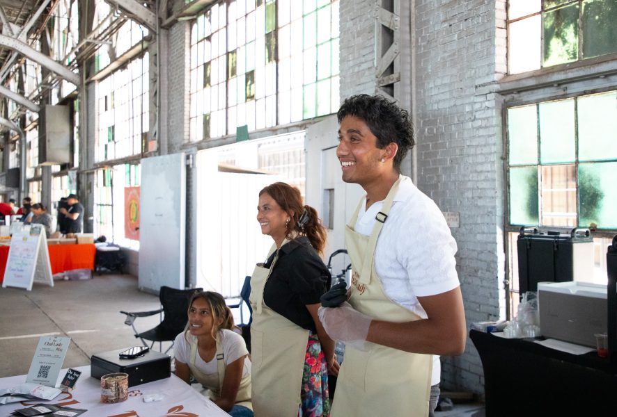 Three vendors smile as people approach their indoor booth at the Rail Yards Market.