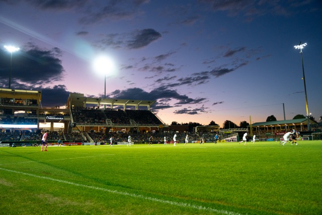 The green pitch is lit by a colorful sunset.