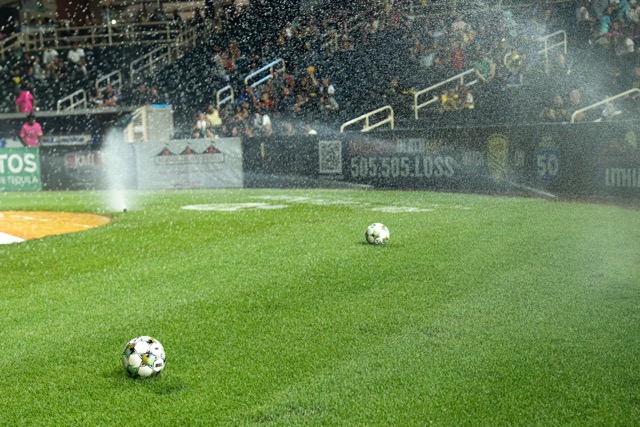Sprinklers refresh the pitch with two soccer balls visible.