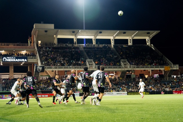 Soccer players look up at a ball in the air.
