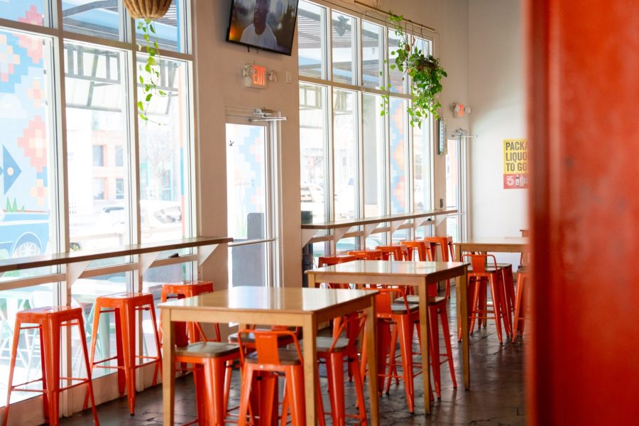 Bright orange stools are places at empty tables, illuminated by the window.