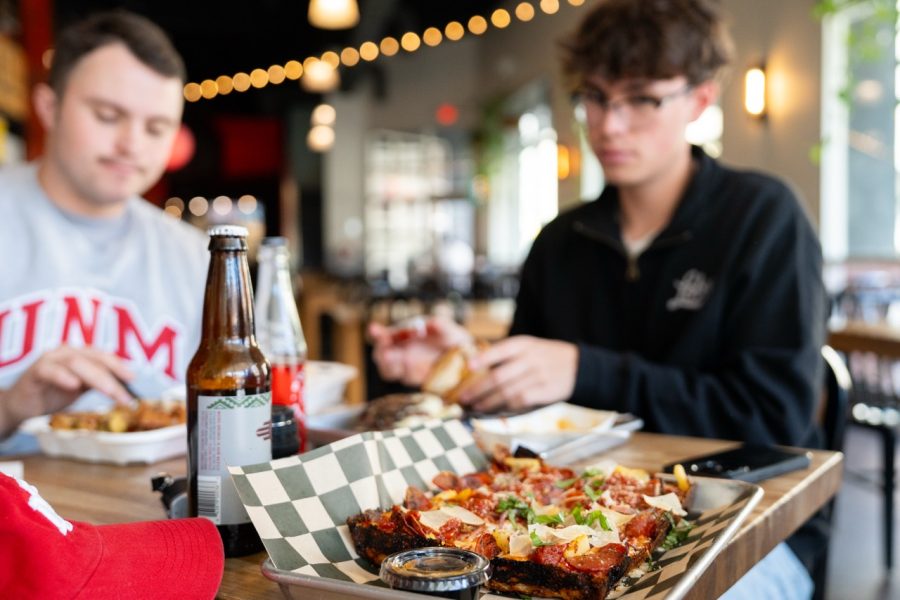 A Thicc Pizza Co. pizza is in the foreground with a Zia soda. Students can be seen eating in the blurred background.