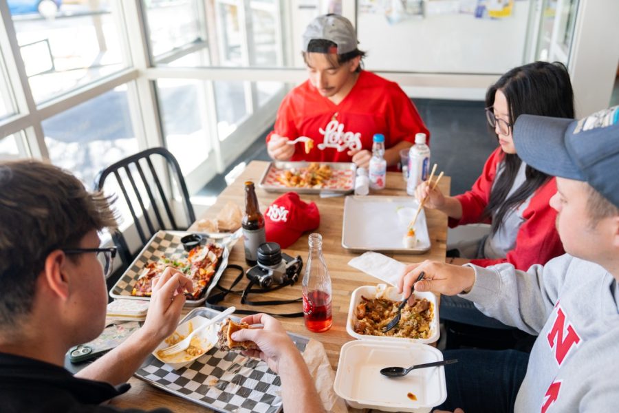 Four students enjoy their meal, lit by large windows.