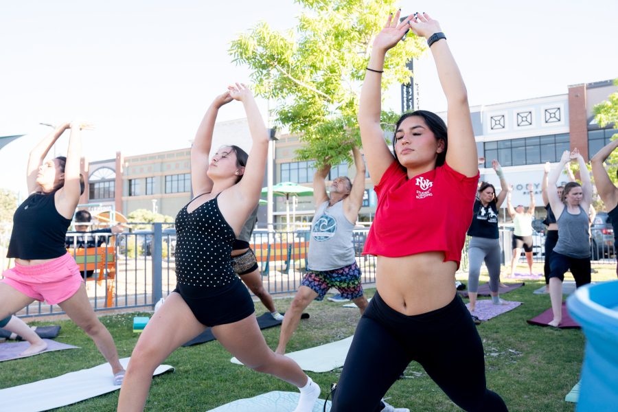 Two UNM students stretch in a yoga pose at a park.