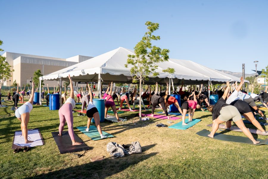 A large group of people do yoga in a park with a large white tent providing shade.