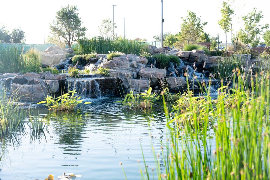 A small body of water with mini rocky waterfalls with a sunny sky.