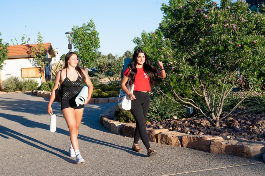 Two UNM students holding yoga mats and water bottles walk along an outdoor path.