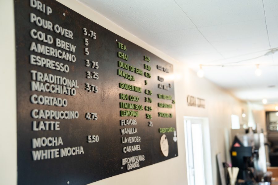 A large menu is hung on a wall with coffee and tea options, including prices and flavors.