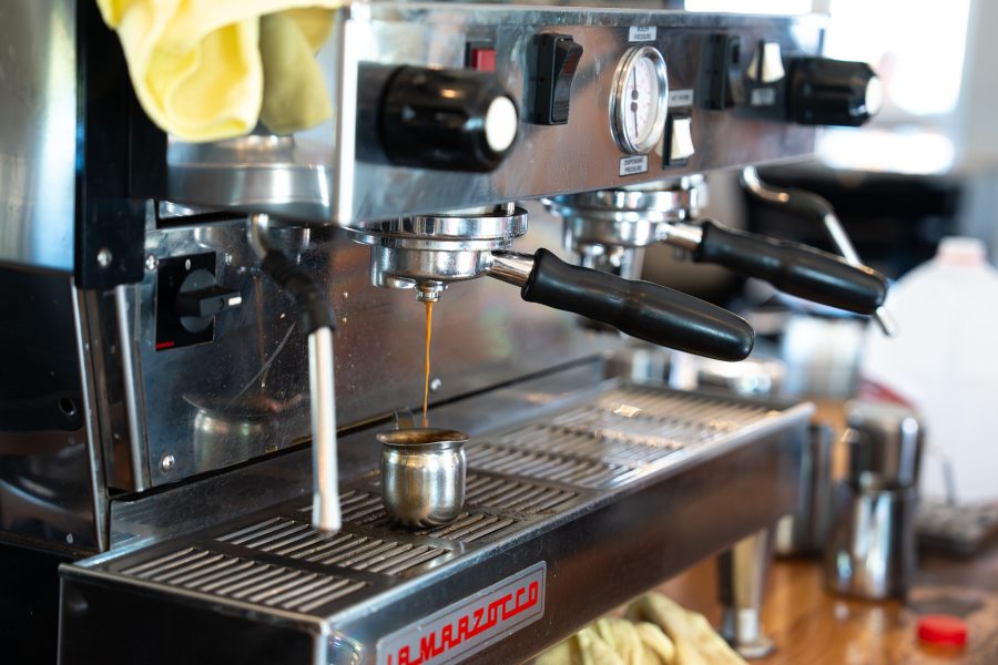 A shiny expresso machine pulls a shot of espresso into a small metal cup.