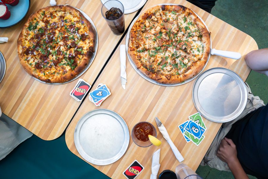 An overhead shot of two wooden tables with two signature pizzas, drinks and UNO cards.