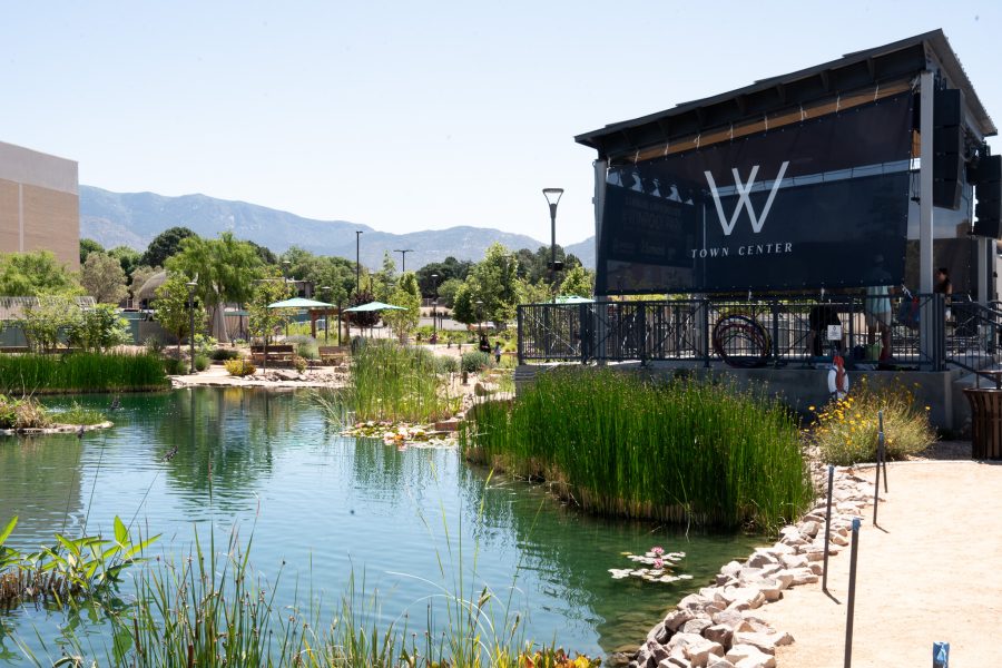 A small body of water with greenery is visible. The Sandia mountains are in the background and there is a large stage with a sign reading “Winrock Town Center”.