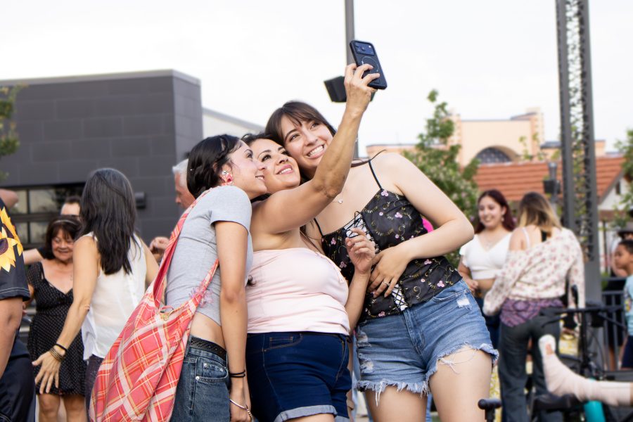 Three people smile while taking a photo together at an outdoor concert.