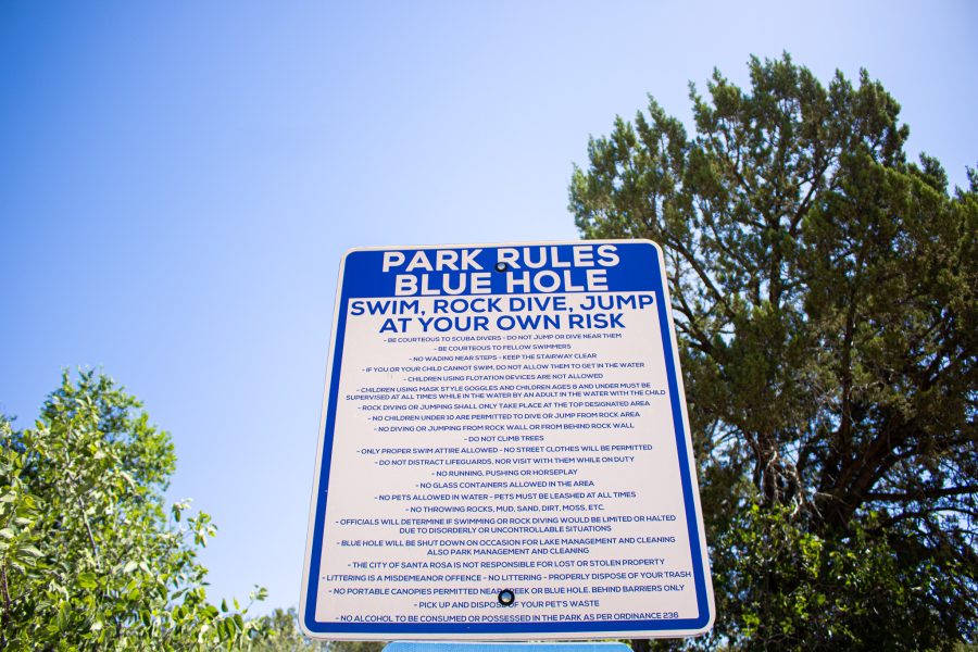 A Blue Hole sign lists rules with a blue sunny sky background.