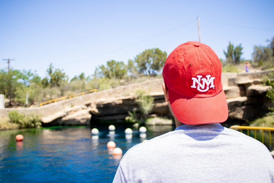 A student wears a backwards cherry UNM hat while looking out at the Blue Hole water.