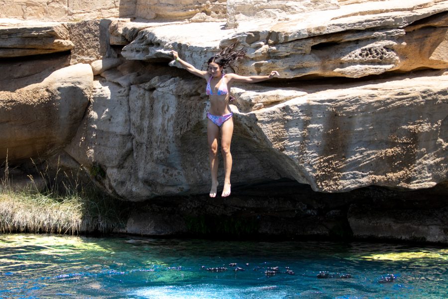 A student jumps off of a rock formation into blue water.