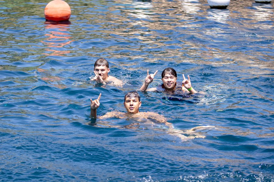 Three students hold up Lobo hand symbols while swimming.